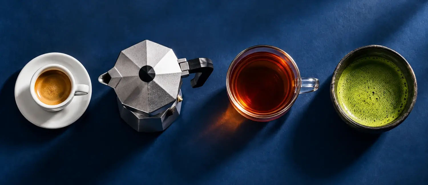 Tazzina di espresso, moka, tazza di tè nero e ciotola di matcha allineate su fondo blu notte