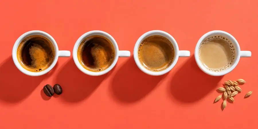 Quattro tazzine in fila: due di espresso, una di decaffeinato e una di orzo chiaro su fondo corallo