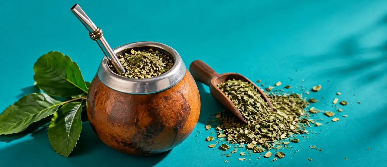 Zucca da mate con bombilla, foglie fresche e una paletta di legno con yerba mate essiccata su fondo turchese