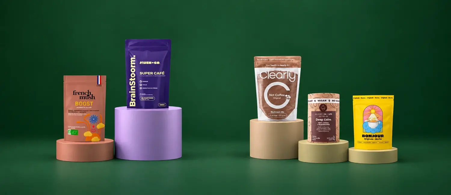 Confezioni di Brainstoorm di Mush N Go, Clearly, French Mush Boost, Mushroom Cups Go Relax e Bonjour Drink su podi rotondi di altezze diverse davanti a un fondo verde scuro
